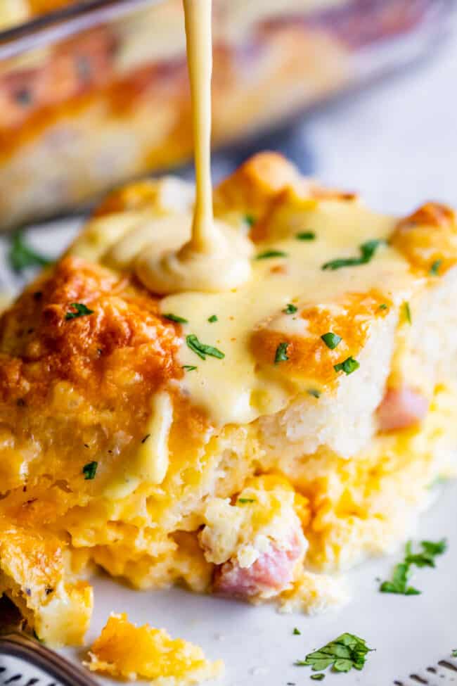 Cheesy Ham and Egg Breakfast Casserole with Biscuits from The Food Charlatan. This crowd-pleasing casserole is my new favorite! Use store bought or homemade biscuits to make a moist and delicious brunch. Top it all off with Hollandaise Sauce for an amazing holiday breakfast! #breakfast #brunch #ham #bacon #sausage #easy #recipe #holidays #Thanksgiving #Christmas #makeahead #withbiscuits #overnight #recipes #foracrowd #best #nightbefore #simple #quick #forlargegroups #Pillsbury #freezer #savory breakfast casserole with biscuits, hollandaise sauce drizzling on top.