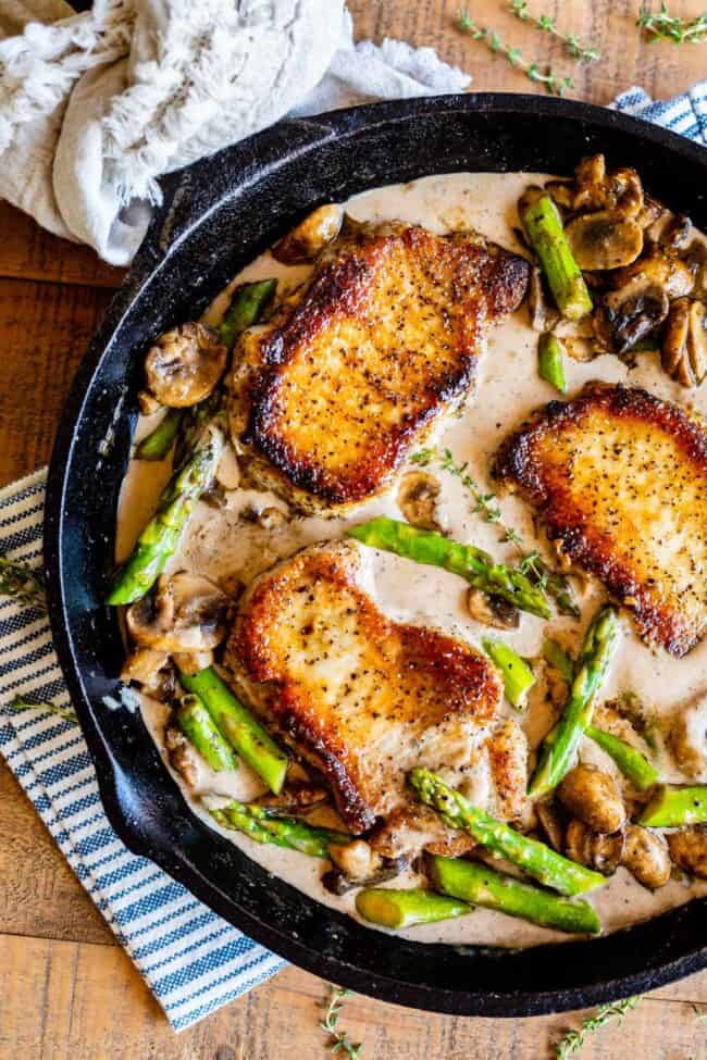 Creamy Pan Seared Pork Chops with Asparagus from The Food Charlatan. Creamy Pan Seared Pork Chops is such an easy weeknight dinner! Juicy boneless pork chops are seared over high heat to get that irresistible crust. Sautéed mushrooms and asparagus in a creamy pan sauce bring it all together. Dinner is done in about 30 minutes! #panseared #porkchop #easy #recipe #boneless #healthy #skillet #balsamic #creamy #asparagus #mushroom #pansauce #onthestove #stovetop #cream #pepper #garlic #weeknight pork chops with asparagus, mushrooms, and a creamy pan sauce in a cast iron skillet.