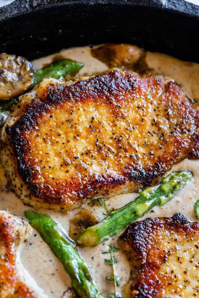 Creamy Pan Seared Pork Chops with Asparagus from The Food Charlatan. Creamy Pan Seared Pork Chops is such an easy weeknight dinner! Juicy boneless pork chops are seared over high heat to get that irresistible crust. Sautéed mushrooms and asparagus in a creamy pan sauce bring it all together. Dinner is done in about 30 minutes! #panseared #porkchop #easy #recipe #boneless #healthy #skillet #balsamic #creamy #asparagus #mushroom #pansauce #onthestove #stovetop #cream #pepper #garlic #weeknight seared pork chops in creamy gravy with mushrooms, asparagus, and fresh thyme.