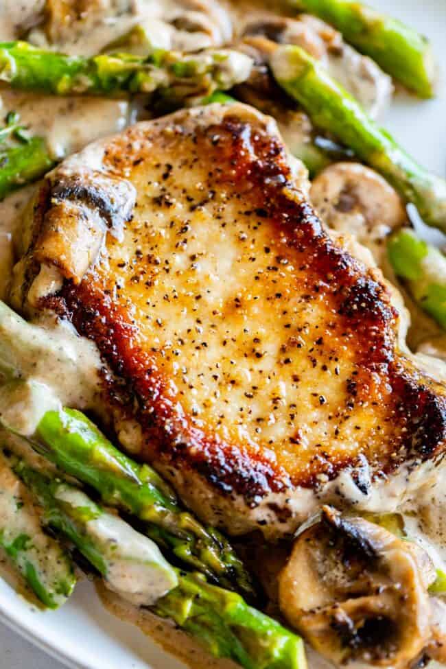 Creamy Pan Seared Pork Chops with Asparagus from The Food Charlatan. Creamy Pan Seared Pork Chops is such an easy weeknight dinner! Juicy boneless pork chops are seared over high heat to get that irresistible crust. Sautéed mushrooms and asparagus in a creamy pan sauce bring it all together. Dinner is done in about 30 minutes! #panseared #porkchop #easy #recipe #boneless #healthy #skillet #balsamic #creamy #asparagus #mushroom #pansauce #onthestove #stovetop #cream #pepper #garlic #weeknight seared boneless pork chops with asparagus and mushroom and a creamy gravy.