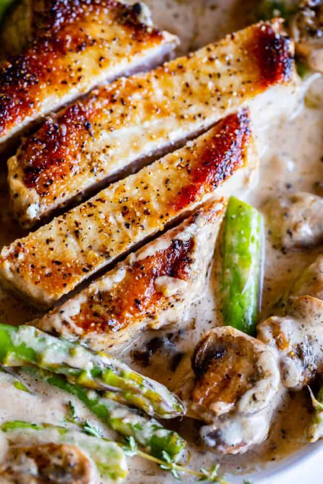 Creamy Pan Seared Pork Chops with Asparagus from The Food Charlatan. Creamy Pan Seared Pork Chops is such an easy weeknight dinner! Juicy boneless pork chops are seared over high heat to get that irresistible crust. Sautéed mushrooms and asparagus in a creamy pan sauce bring it all together. Dinner is done in about 30 minutes! #panseared #porkchop #easy #recipe #boneless #healthy #skillet #balsamic #creamy #asparagus #mushroom #pansauce #onthestove #stovetop #cream #pepper #garlic #weeknight sliced pan seared pork chops with mushrooms, asparagus, and a creamy pan gravy.