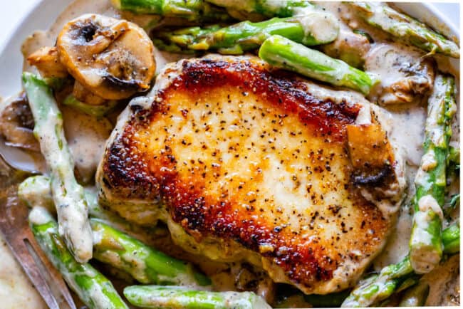 pork chop with creamy gravy, mushrooms, and asparagus.