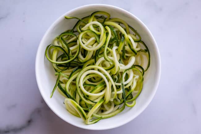 zoodles in a white bowl on a countertop shot from overhead.
