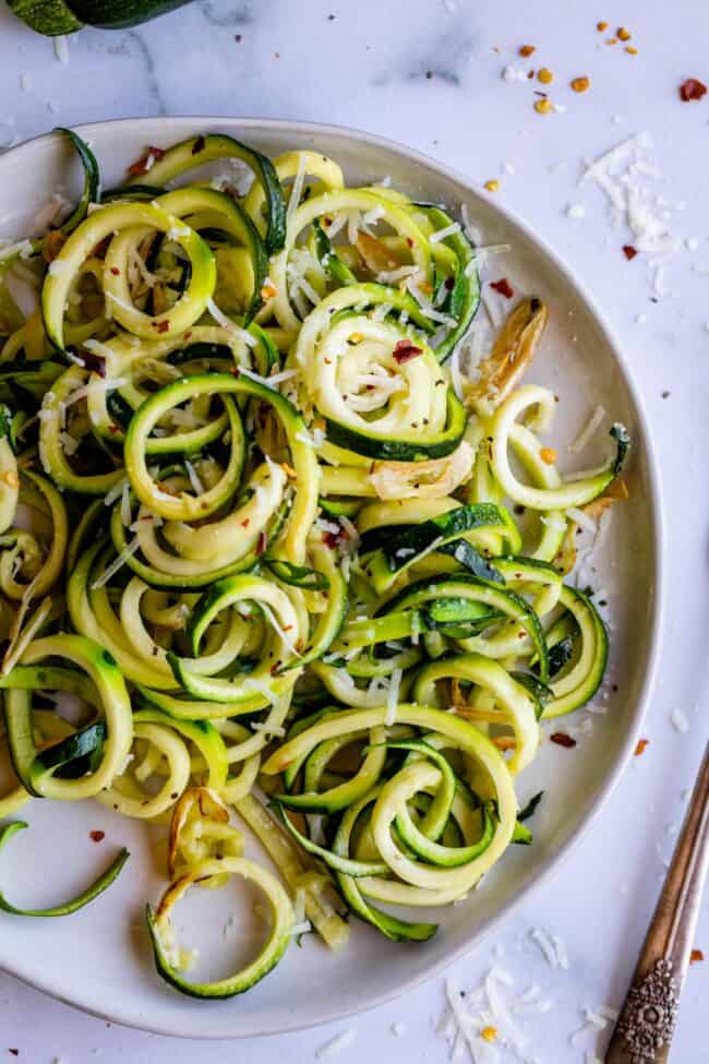 zucchini noodles on a white plate with spices and cheese. 