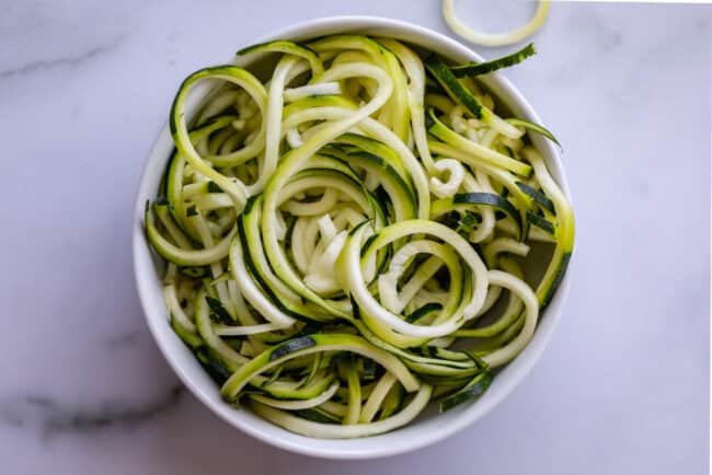 curly zoodles in a white bowl on a counter.