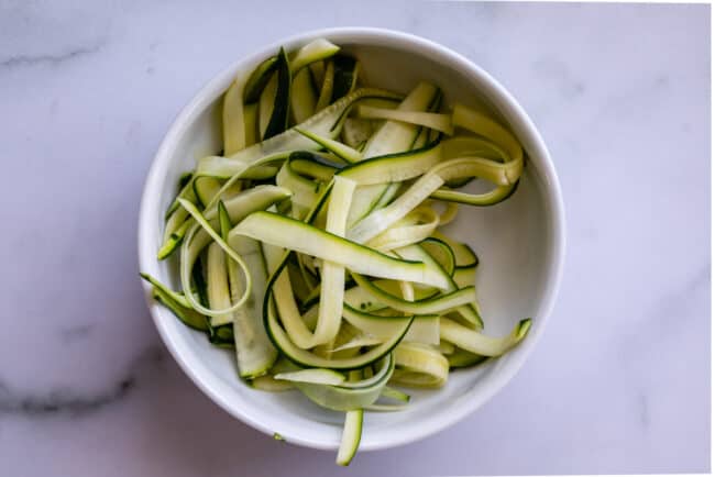 zucchini ribbons in a white bowl, made from a vegetable peeler.