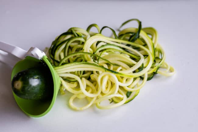 a zucchini being turned into zoodles using a handheld device.