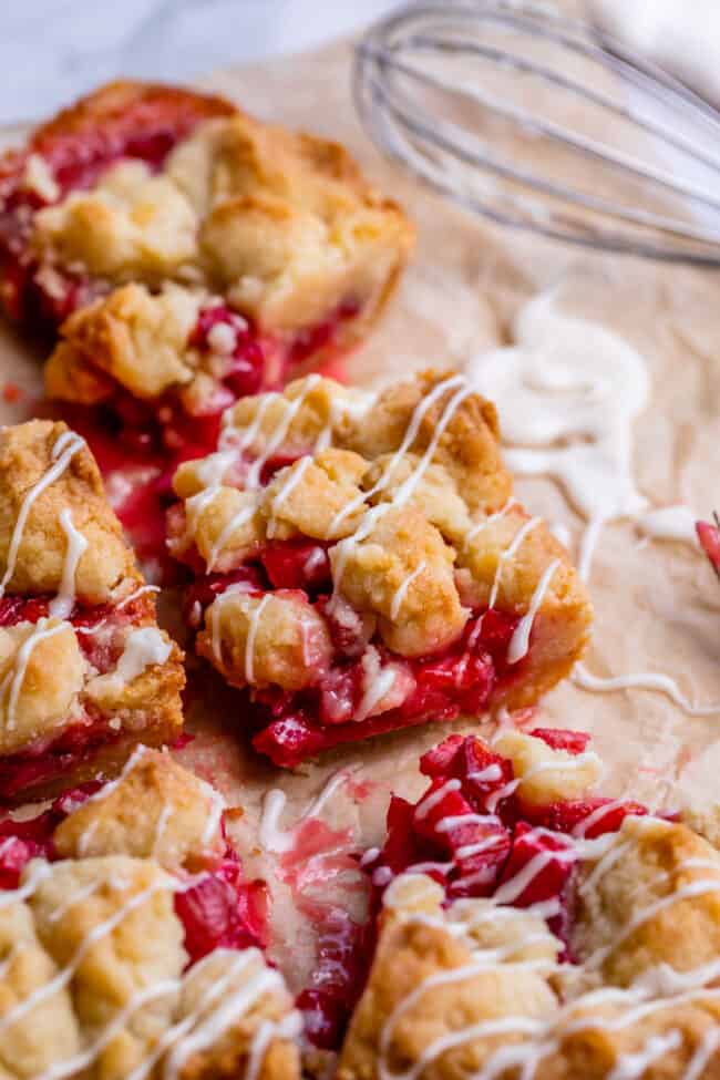 Rhubarb Shortbread Bars from The Food Charlatan. Rhubarb Shortbread Bars are a dream come true! A thick and buttery shortbread crust, topped with a layer of simple rhubarb filling, and topped with even more glorious shortbread. There is a secret ingredient in this recipe that makes these rhubarb bars bright ruby red, and it's not food coloring. It works like a charm! #easy #recipe #rhubarb #shortbread #butter #bars #dessert #withoutstrawberry #recipe #shortbreadcrust #lemon #best #pie rhubarb bars drizzled with glaze