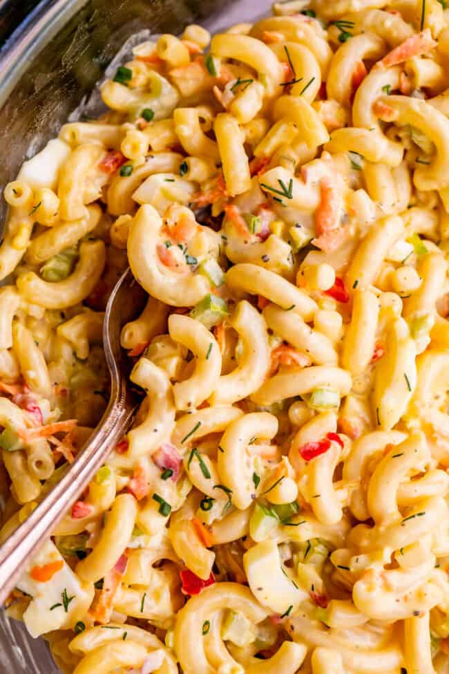 moist macaroni salad in a clear mixing bowl with serving spoon.