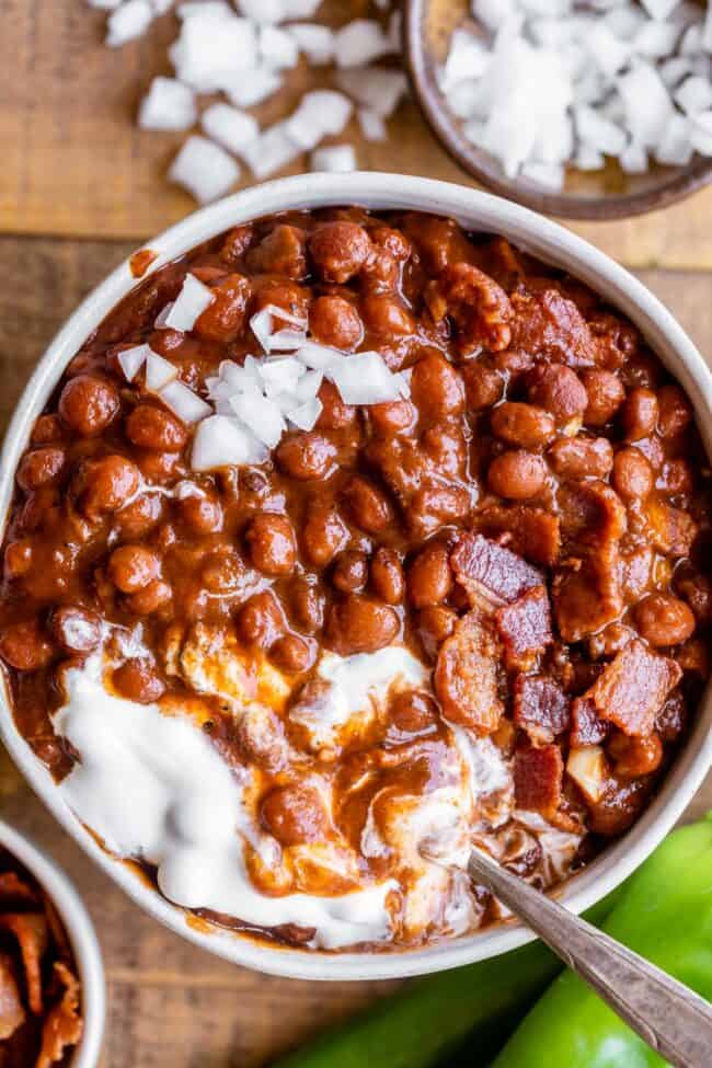 Santa Maria Pinquito Beans from The Food Charlatan. These Santa Maria style Pinquito Beans are the perfect summer barbecue side dish! Originally created in Santa Maria, California to be served alongside Grilled Tri Tip, these beans are smokey and sweet with the perfect blend of spices. Eat them with tri tip or serve alongside whatever else you're barbecuing this summer! #easy #recipe #bbq #barbecue #beans #bakedbeans #santamaria #tritip #sidedish #bacon #pinquito #creamy #summer #onion #anaheim pinquito beans in a bowl with sour cream and chopped onions.