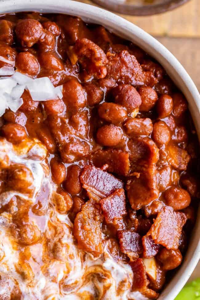Santa Maria Pinquito Beans from The Food Charlatan. These Santa Maria style Pinquito Beans are the perfect summer barbecue side dish! Originally created in Santa Maria, California to be served alongside Grilled Tri Tip, these beans are smokey and sweet with the perfect blend of spices. Eat them with tri tip or serve alongside whatever else you're barbecuing this summer! #easy #recipe #bbq #barbecue #beans #bakedbeans #santamaria #tritip #sidedish #bacon #pinquito #creamy #summer #onion #anaheim santa maria style beans in a bowl with bacon and sour cream.
