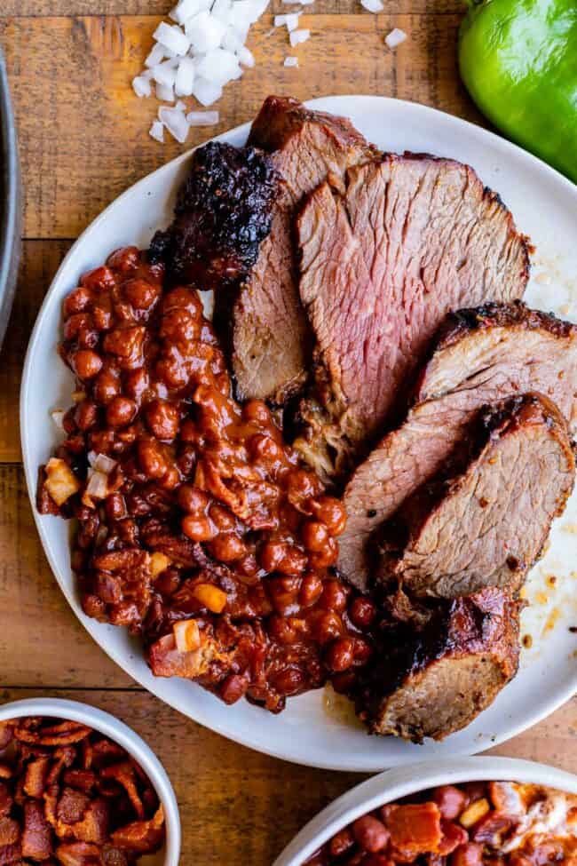 Santa Maria Pinquito Beans from The Food Charlatan. These Santa Maria style Pinquito Beans are the perfect summer barbecue side dish! Originally created in Santa Maria, California to be served alongside Grilled Tri Tip, these beans are smokey and sweet with the perfect blend of spices. Eat them with tri tip or serve alongside whatever else you're barbecuing this summer! #easy #recipe #bbq #barbecue #beans #bakedbeans #santamaria #tritip #sidedish #bacon #pinquito #creamy #summer #onion #anaheim santa maria pinquito beans with tri tip on a plate.