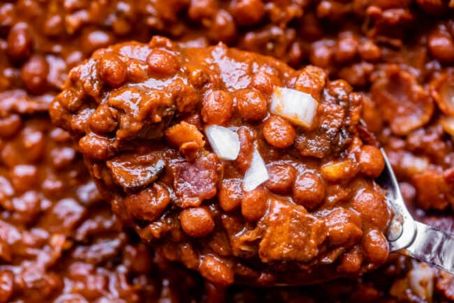 Santa Maria Pinquito Beans from The Food Charlatan. These Santa Maria style Pinquito Beans are the perfect summer barbecue side dish! Originally created in Santa Maria, California to be served alongside Grilled Tri Tip, these beans are smokey and sweet with the perfect blend of spices. Eat them with tri tip or serve alongside whatever else you're barbecuing this summer! #easy #recipe #bbq #barbecue #beans #bakedbeans #santamaria #tritip #sidedish #bacon #pinquito #creamy #summer #onion #anaheim santa maria pinquito beans on a spoon.