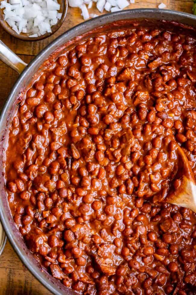 Santa Maria Pinquito Beans from The Food Charlatan. These Santa Maria style Pinquito Beans are the perfect summer barbecue side dish! Originally created in Santa Maria, California to be served alongside Grilled Tri Tip, these beans are smokey and sweet with the perfect blend of spices. Eat them with tri tip or serve alongside whatever else you're barbecuing this summer! #easy #recipe #bbq #barbecue #beans #bakedbeans #santamaria #tritip #sidedish #bacon #pinquito #creamy #summer #onion #anaheim pinquito beans in a pan with a spoon.