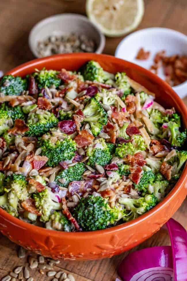 Broccoli and bacon salad in an orange bowl with red onion and a lemon.