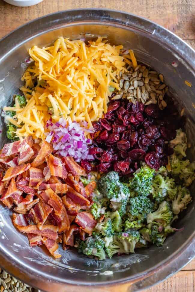 cheddar, sunflower seed, cranberry, broccoli, bacon, and red onion in a metal bowl.