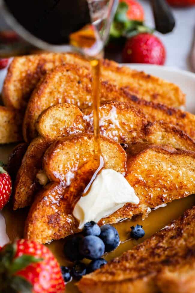 syrup poured over a stack of French toast, with strawberries and blueberries.