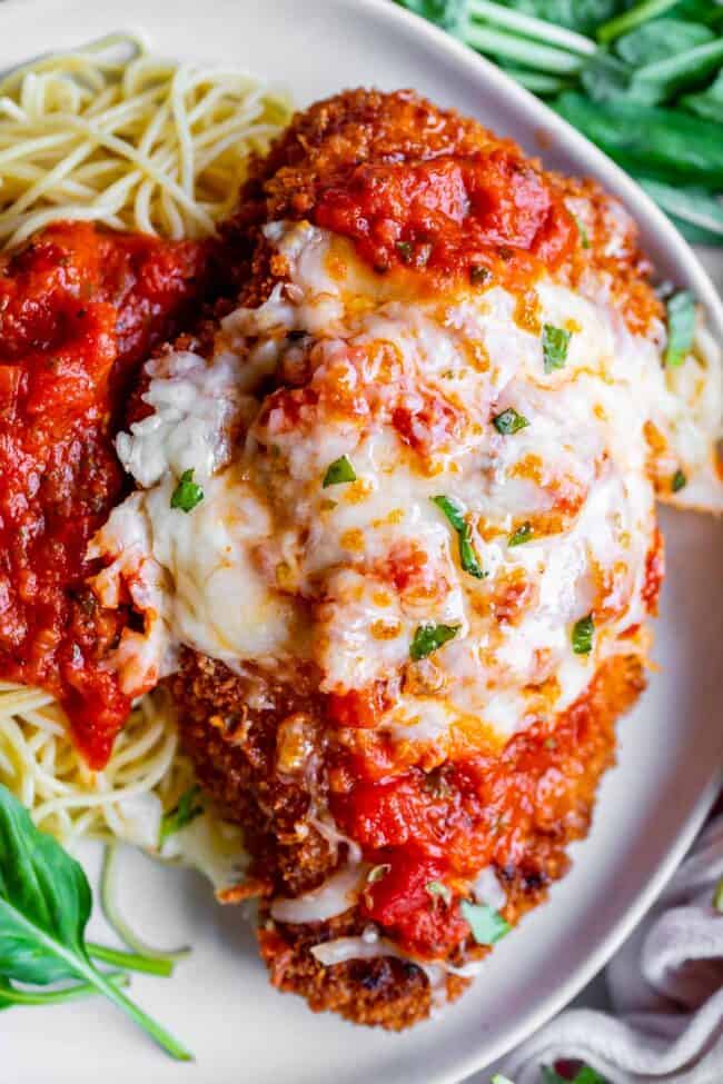 crispy parmesan chicken on a plate with pasta and marinara sauce.