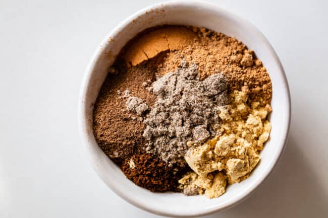 spices including nutmeg, ginger, cloves, allspice, and cardamom in a bowl.