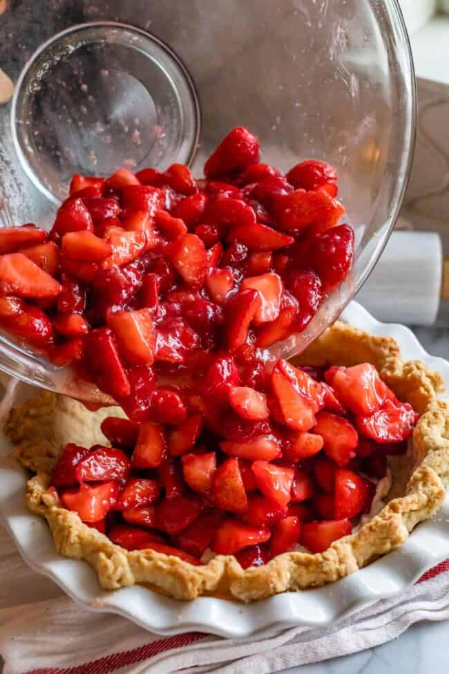 pouring strawberries into a pre baked pie shell.