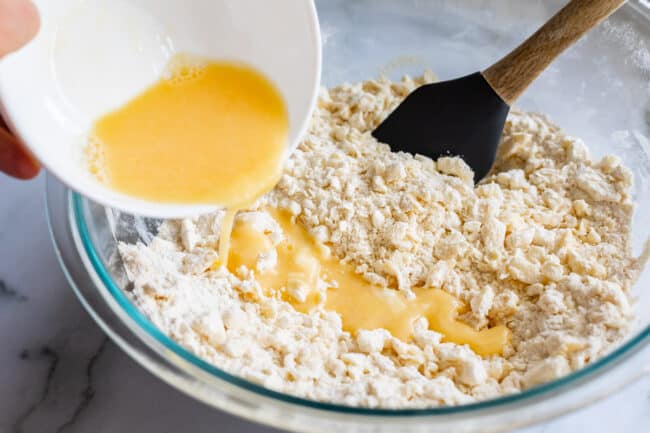 pouring egg and ice water into pie crust dough.