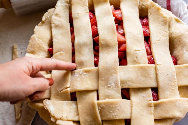 finger pointing to the next strip of pie dough that needs to be pulled back for lattice crust