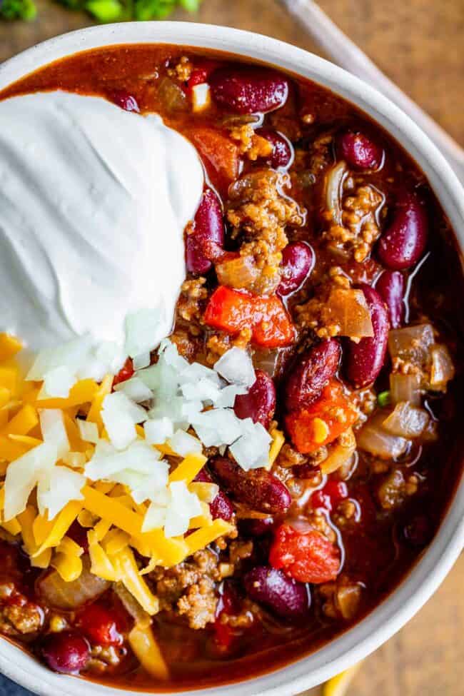 basic chili recipe in a white bowl garnished with sour cream, cheese, onions.