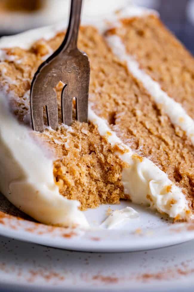 spice cake with cream cheese frosting on a white plate with a fork in the cake and a bite removed.