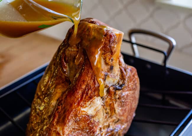 pouring honey glaze over a spiral ham.