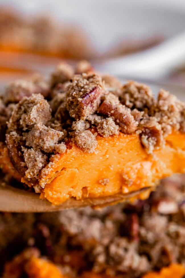 sweet potato casserole with pecans being lifted from the pan on a spoon.
