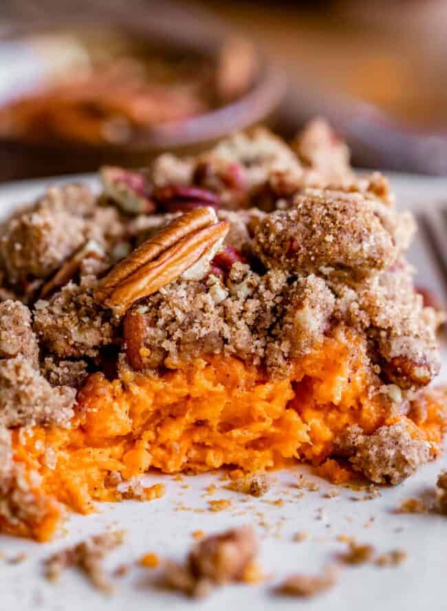 sweet potato casserole with pecan topping on a plate with bites taken out.