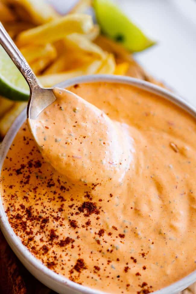 spoon lifting chipotle mayo recipe from a bowl sprinkled with chipotle powder.