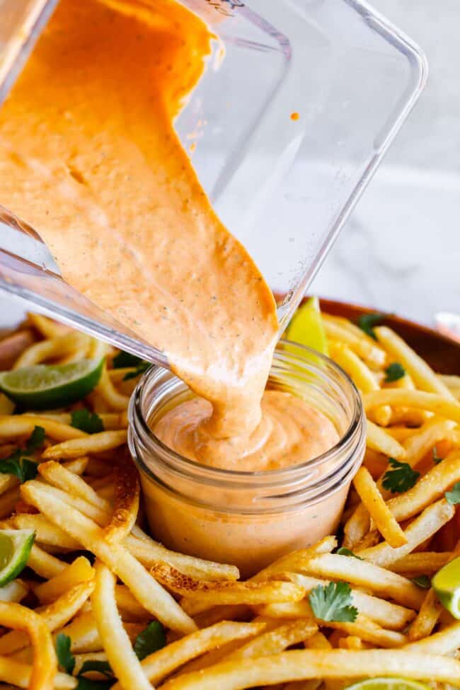 pouring chipotle mayo sauce into a mason jar surrounded by fries.