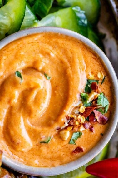 thai peanut sauce recipe in a bowl sprinkled with cilantro, dried chili, and cucumbers on the side