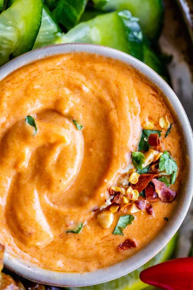thai peanut sauce recipe in a bowl sprinkled with cilantro, dried chili, and cucumbers on the side.
