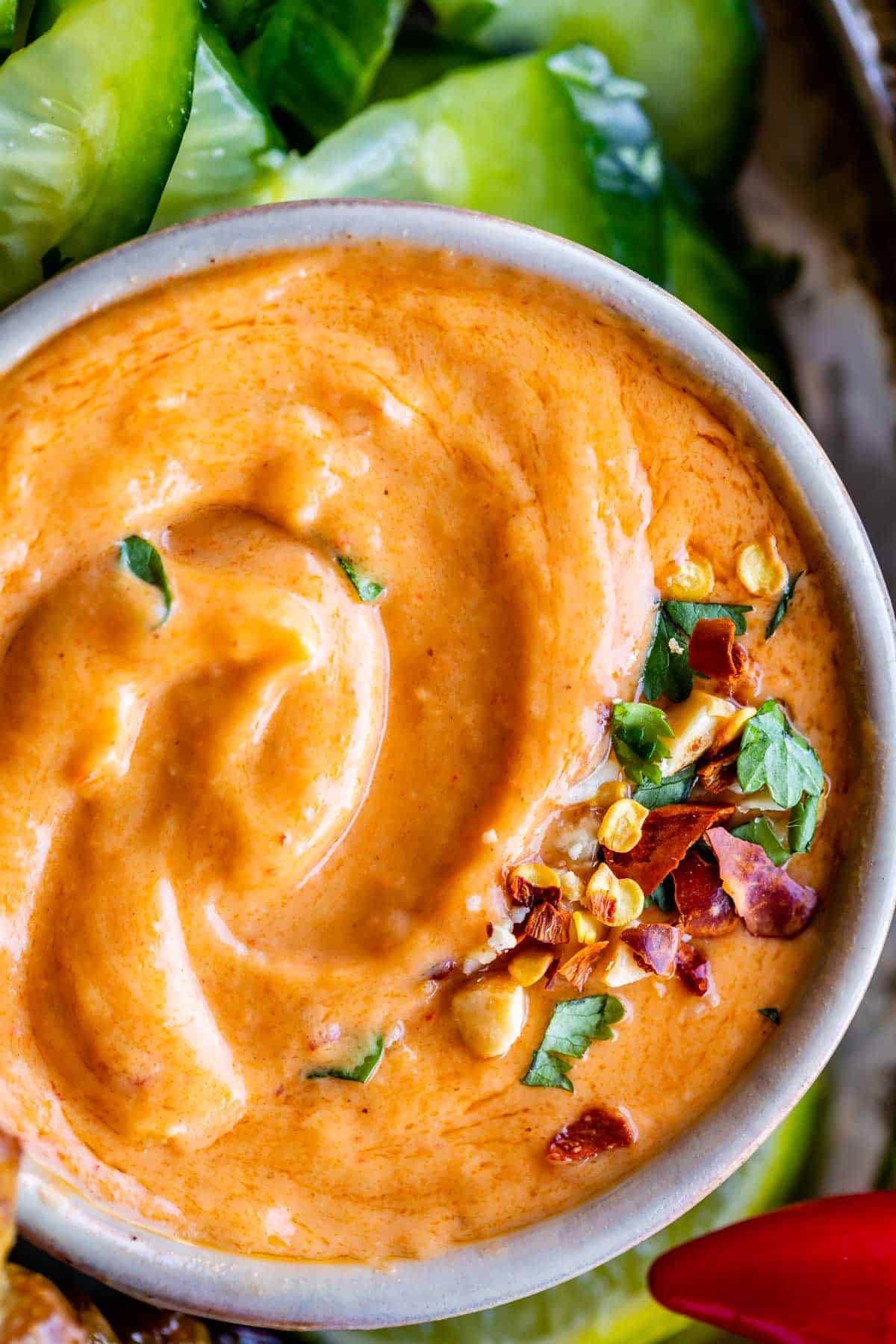thai peanut sauce recipe in a bowl sprinkled with cilantro, dried chili, and cucumbers on the side