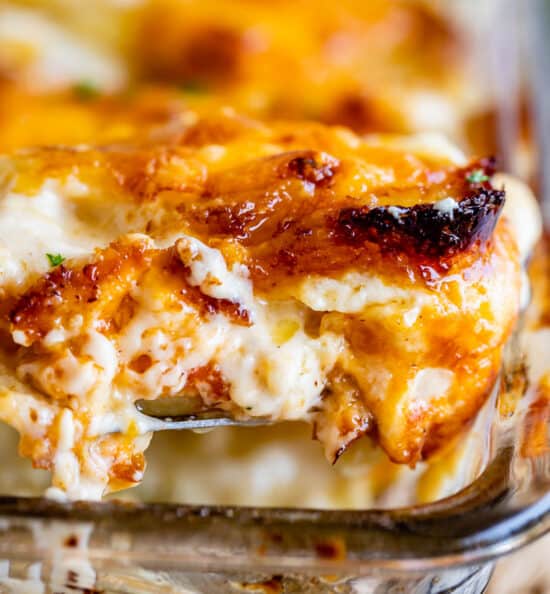 scalloped potatoes with crispy edges being lifted from a clear casserole dish