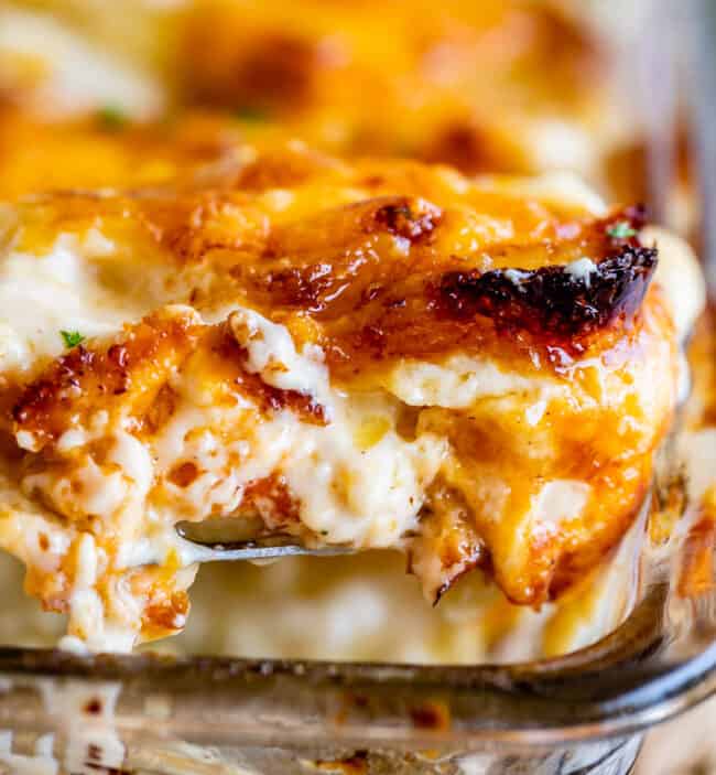cheese scalloped potatoes with crispy edges being lifted from a clear casserole dish.