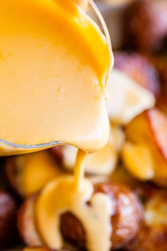 pouring cheese sauce over roasted potatoes.