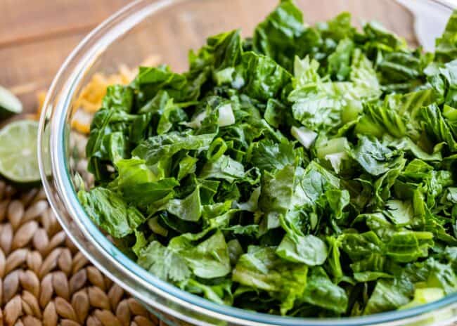 a glass bowl of chopped lettuce with cilantro and green onions.
