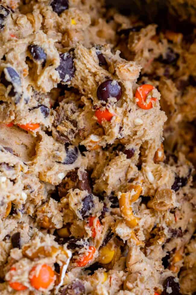 raw peanut butter cookie dough in a bowl with Reese's pieces, pretzels, peanut butter chips, and chocolate chips.