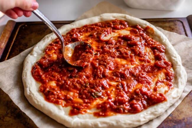 spreading pizza sauce on pizza dough