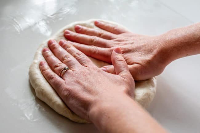 two hands pressing down pizza dough