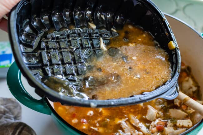 adding broth from a plastic pan to a pot of chili.