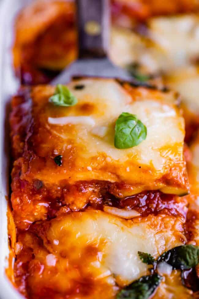 cheesy zucchini lasagna being lifted from the pan with a spatula, topped with basil.