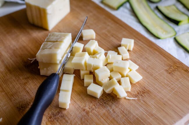 mozzarella cheese on a wooden cutting board because chopped into chunks with a knife.