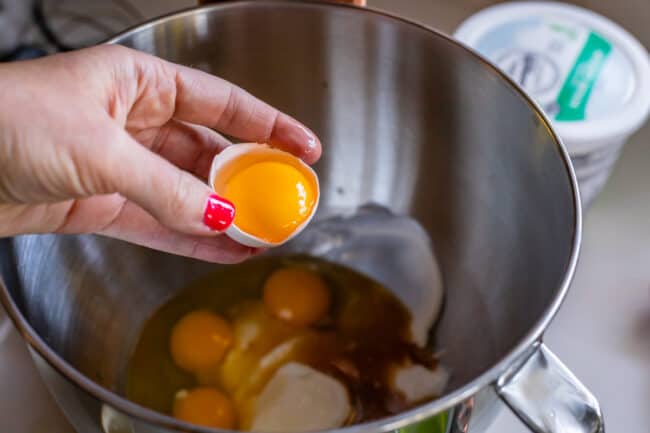 adding egg yolk to a stand mixer bowl with sour cream.