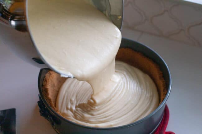 Pouring cheesecake batter into graham crust in springform pan.