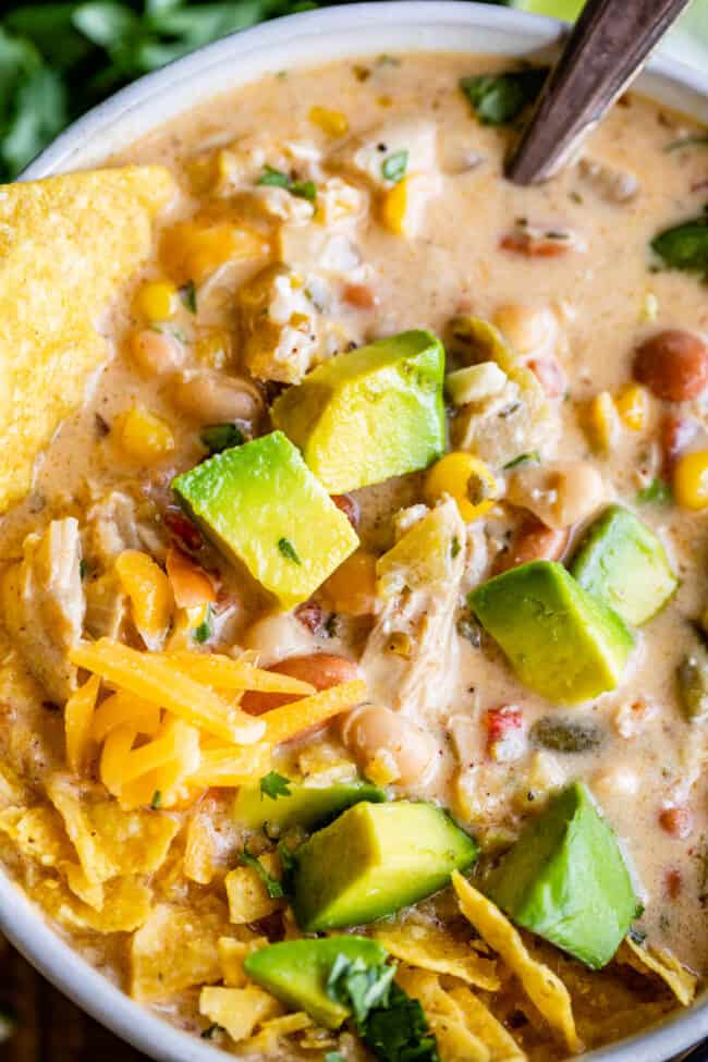 easy white chicken chili close up in a bowl with tortilla chips and avocado.