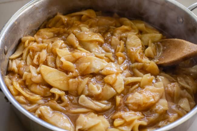 cooked apple pie filling in a pan being stirred with a wooden spoon.